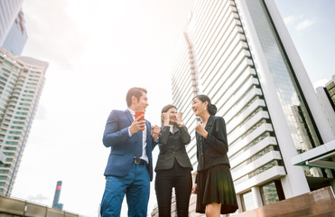 Celebrating success. Low angle view of excited young businessman and business woman keeping arms raised and expressing positive while standing outdoors with office building in the background