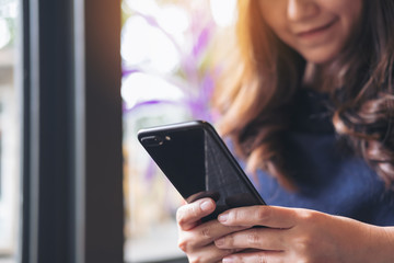 A beautiful Asian woman with smiley face using and looking at a black smart phone in modern loft cafe