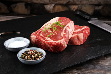 Raw fresh meat Ribeye Steak, seasoning and meat fork on dark background