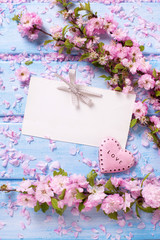 Pink  sakura flowers, empty tag and  heart on blue wooden planks.