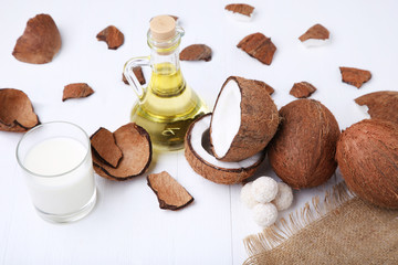 Coconuts with candies and bottle of oil on white wooden table
