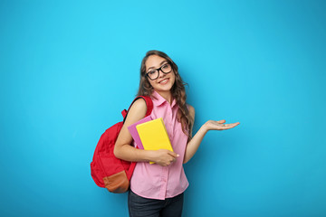 Portrait of student girl with backpack and books on blue background