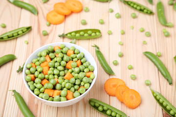 Green peas and carrots sliced in bowl on wooden table