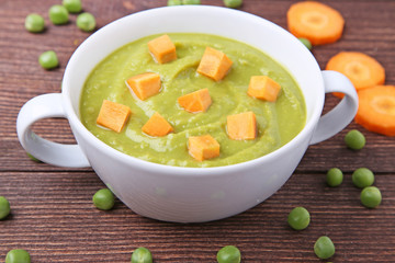 Green peas soup in plate with carrot on wooden table