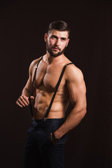 Young handsome muscular man with a beard, posing on a black background