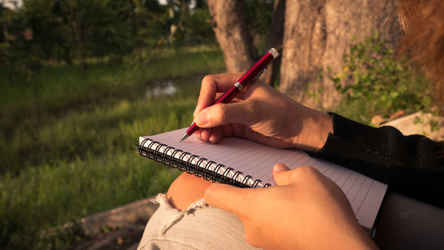 Young woman with pen writing on notebook at nature.