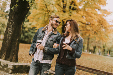 Young couple walking with coffee cups in the autumn park