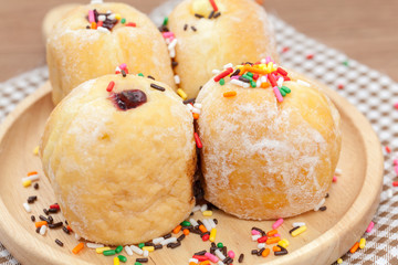 a variety of jam doughnut on wooden plate with sprinkles