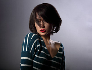 Beautiful enjoing woman moving and shaking her short black hair style with red lipstick on grey background in fashion pullover