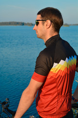 A cyclist in gear near the lake enjoys a summer sunset. Hobbies, sports