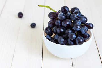 Black grape branch in bowl on white wooden background