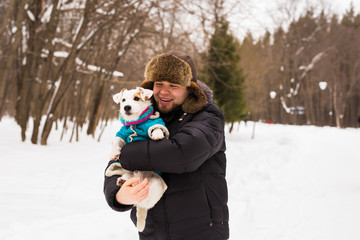 Pet owner, dog, and people concept - Young smiling caucasian man holding Jack Russell terrier outdoor in winter time.