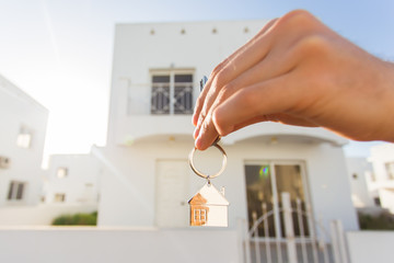 Holding house keys on house shaped keychain closeup in front of a new home. Concept of real estate