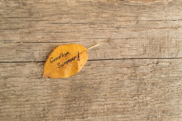 Yellow or orange leaf with inscription GOODBUE SUMMER on the old wooden background