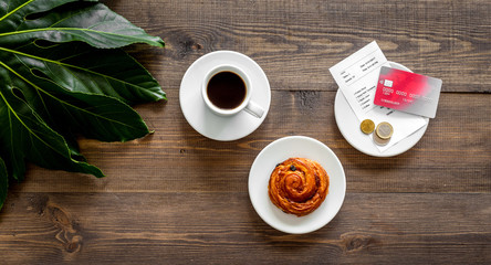 Restaurant bill and bank card near cup of coffee on dark wooden table top view copyspace