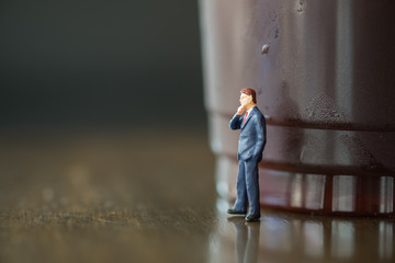 Businessman miniature people figure standing and thinking on wooden table with plastic cup of iced black coffee. Using as business, planning and working concept.