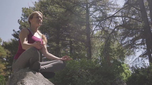 Young Woman Practices Meditation And Mindfulness On A Boulder In Nature