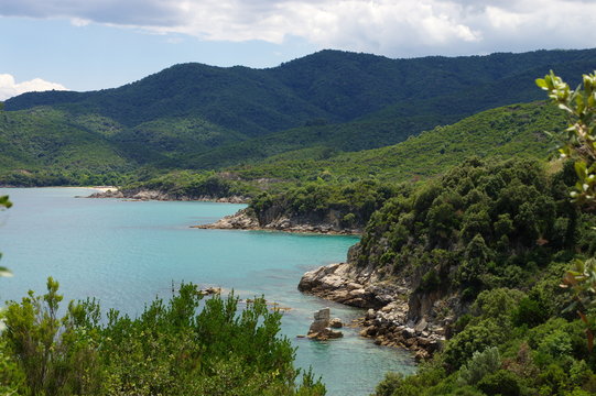 Sea coast near Stagria, Greece. Cliffs covered with lush plants. A blue sky with white clouds can be seen above the azure sea.
