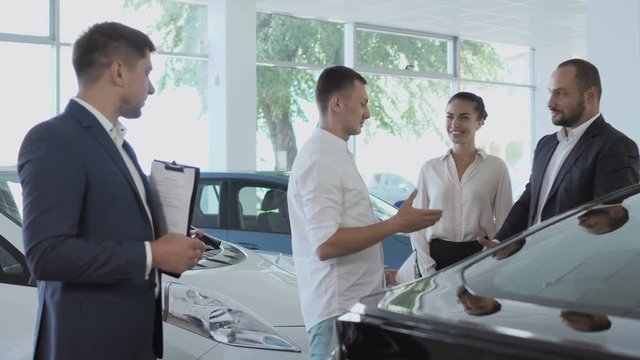 The salesman greets the couple with car purchase in the car showroom
