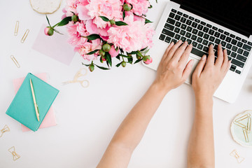 Flat lay home office desk. Workspace with woman hands, laptop, pink peony bouquet, golden accessories, mint diary. Top view