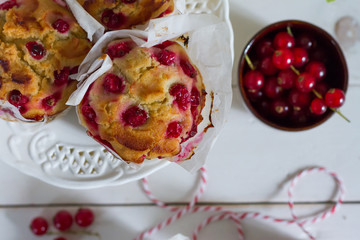 Red currant muffins on white plateau. White wooden table, gray background. Baking paper.