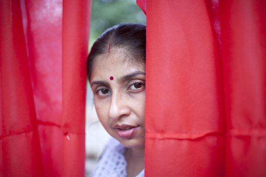 Happy Indian woman peeping through red curtain