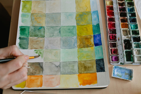closeup of hands of artist creating mixing chart with watercolor