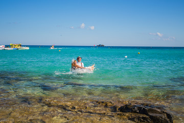 Fototapeta na wymiar Happy couple swims after wedding in turquoise sea. Romantic newly-married couple enjoying a summer vacation.