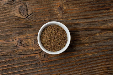 Cumin in white bowl on an old wooden table