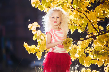 A little girl who smiles on a background of yellow leaves