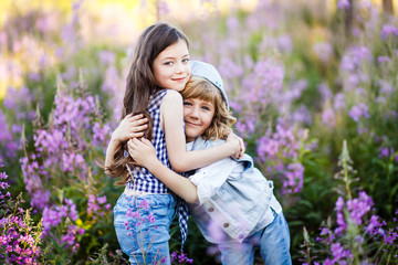 Brother and sister hugging at sunset in the field of purple flowers and having fun outside. Family, friendship, and happiness concept