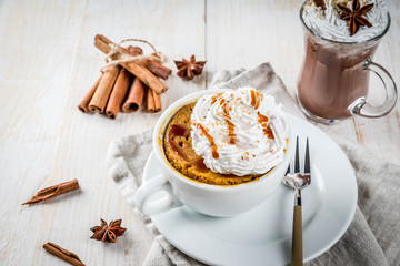 Recipes with pumpkins, fast food, microwave meal. Spicy pumpkin pie in mug, with whipped cream, ice cream, cinnamon, anise. On white wooden table, with cup of hot chocolate. Copy space