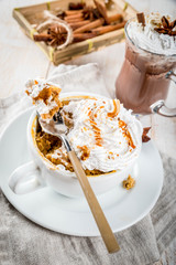 Recipes with pumpkins, fast food, microwave meal. Spicy pumpkin pie in mug, with whipped cream, ice cream, cinnamon, anise. On white wooden table, with cup of hot chocolate. Copy space