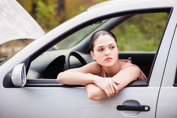 Young woman waits for assistance near her car, which broken down on the road side