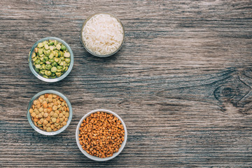 Rice, buckwheat, peas and lentils in small cups on a wooden surface.