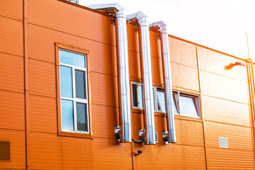 The facade of an industrial building. The building is orange with air conditioning, ventilation pipes and a metal staircase to the roof