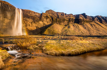 The Seljalandfoss water fall and a small water fall face to sunset with the brown grass in Iceland.