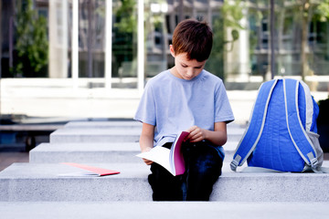 Child flipping through book pages. Boy reading book and doing homework outdoors