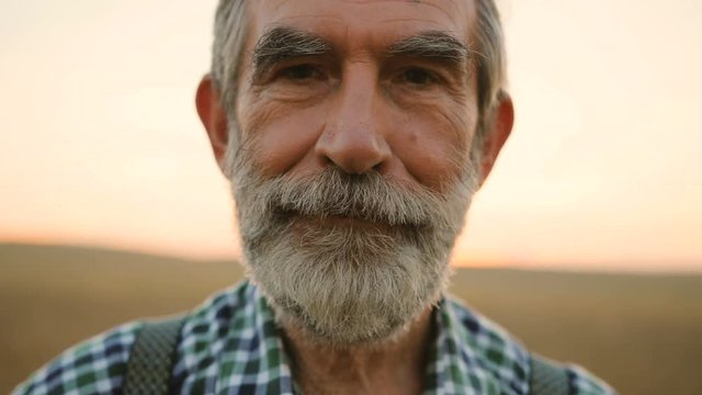 Close up portrait of happy fermer with beard smiling on camera in the golden field on the sky background.