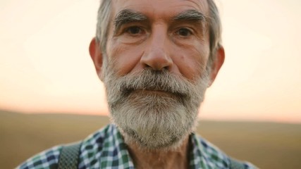 Close up portrait of senior man with beard looking to the camera in the golden field on the sky background. - Powered by Adobe