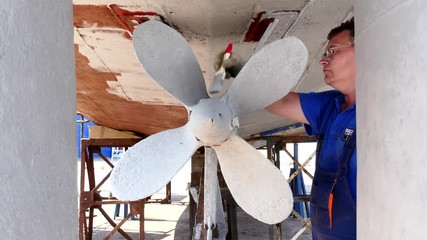 Worker paints metal of old rusty ship propeller at shipyard in port of Moscow. Process of repair and reconstruction of sea vessel. Technology of manual painting boats. Industry of water transport. - Powered by Adobe