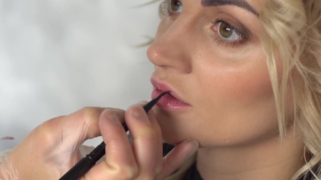 Makeup artist paints the lips of a young woman in a beauty salon, close-up