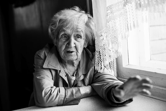 Elderly woman gesturing with hands while sitting at the table. Black and white photography.