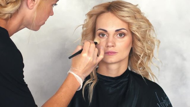 The make-up artist puts a blush on the face of a young woman, close up
