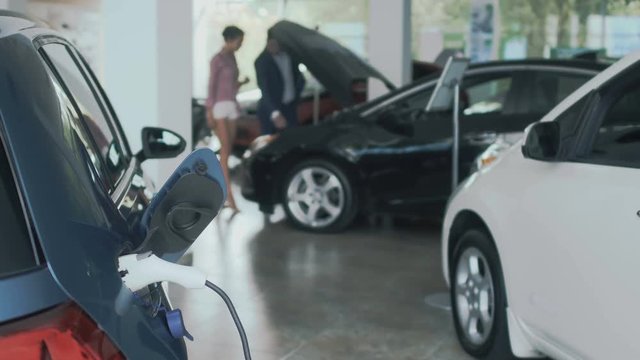 Charging of electric car, people opens the hood of car on blurred background