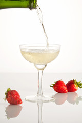 Pouring champagne into the glass standing on the white glass table