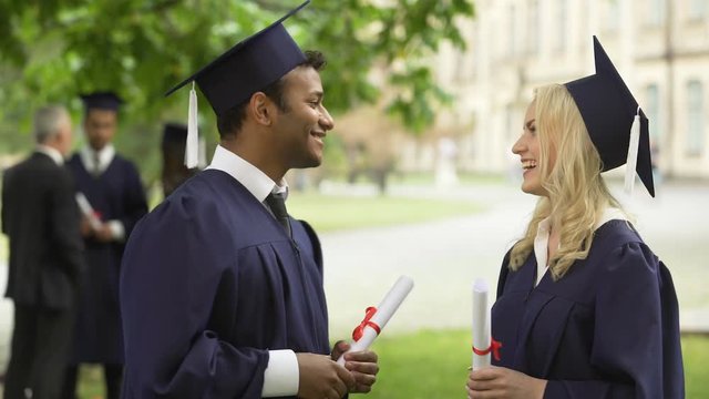 Graduate students with diplomas talking, high-fiving each other, convocation day
