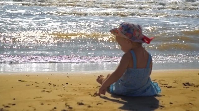 Little girl is sitting on a sandy beach and is painting on the sand