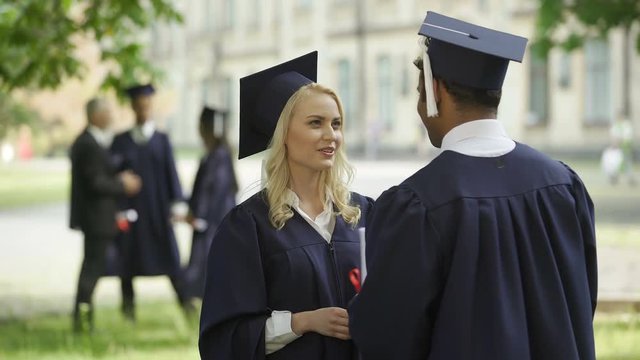 Female graduate in square hat with diploma talking to classmate, convocation day