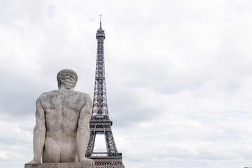 Fototapeta na wymiar Paris France Eiffel Tower close-up with stone statue of seated man from the back looking at dusk sky